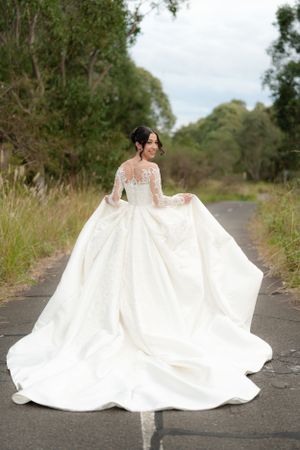 Bride in voluminous long-sleeve lace ball gown twirls joyfully on a quiet road surrounded by Australian bushland.