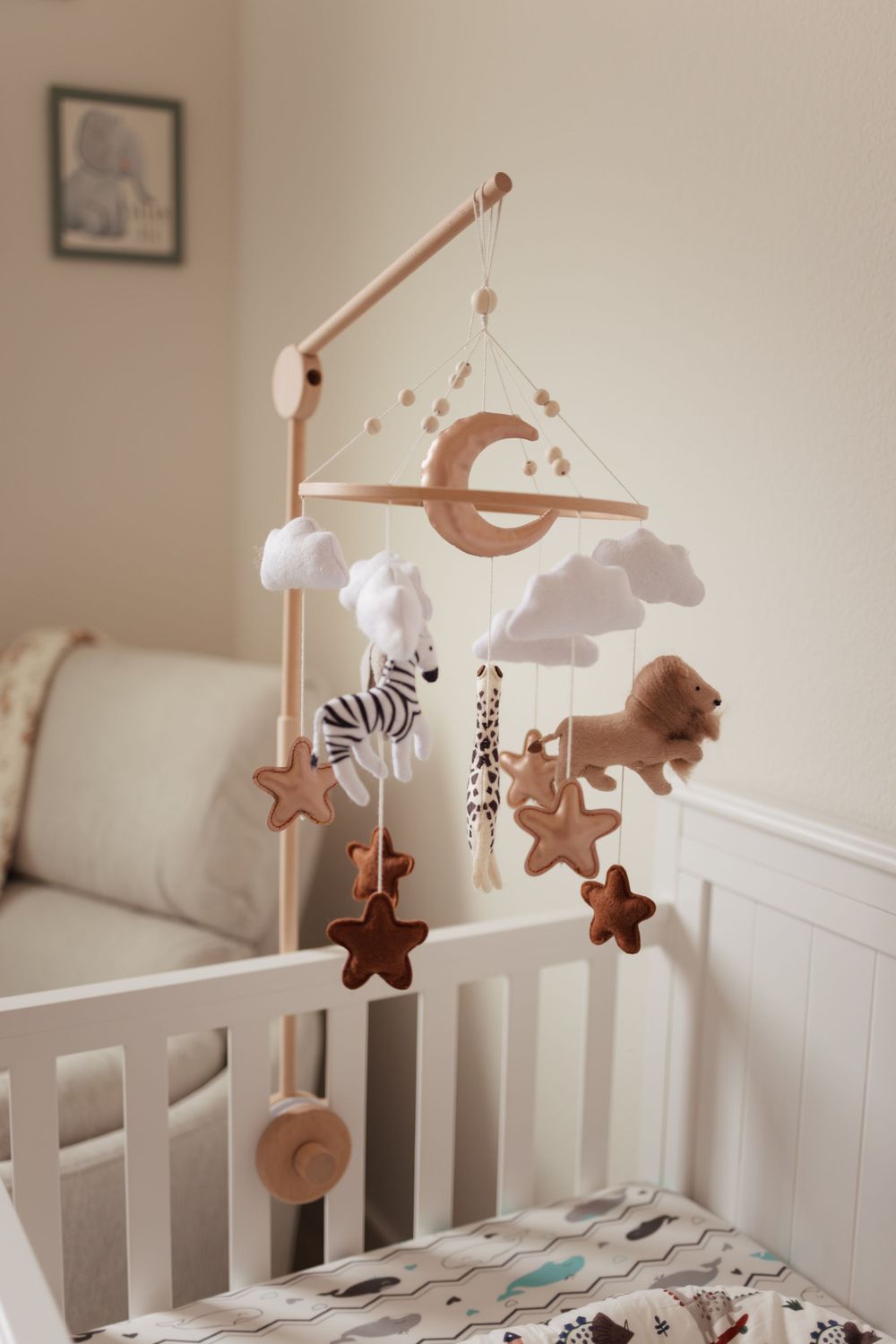 A wooden baby mobile with plush animals, clouds, stars and moon hangs above a white crib in a nursery.