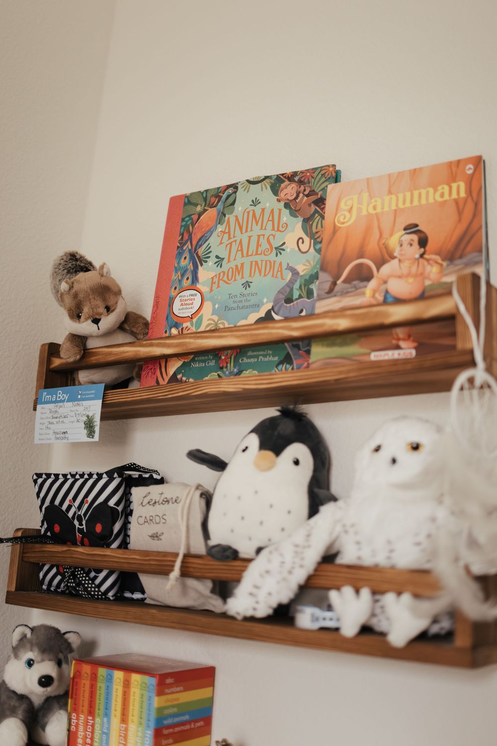 Wooden floating shelves display children's books, stuffed animals including a penguin and polar bear, and colorful decor items.