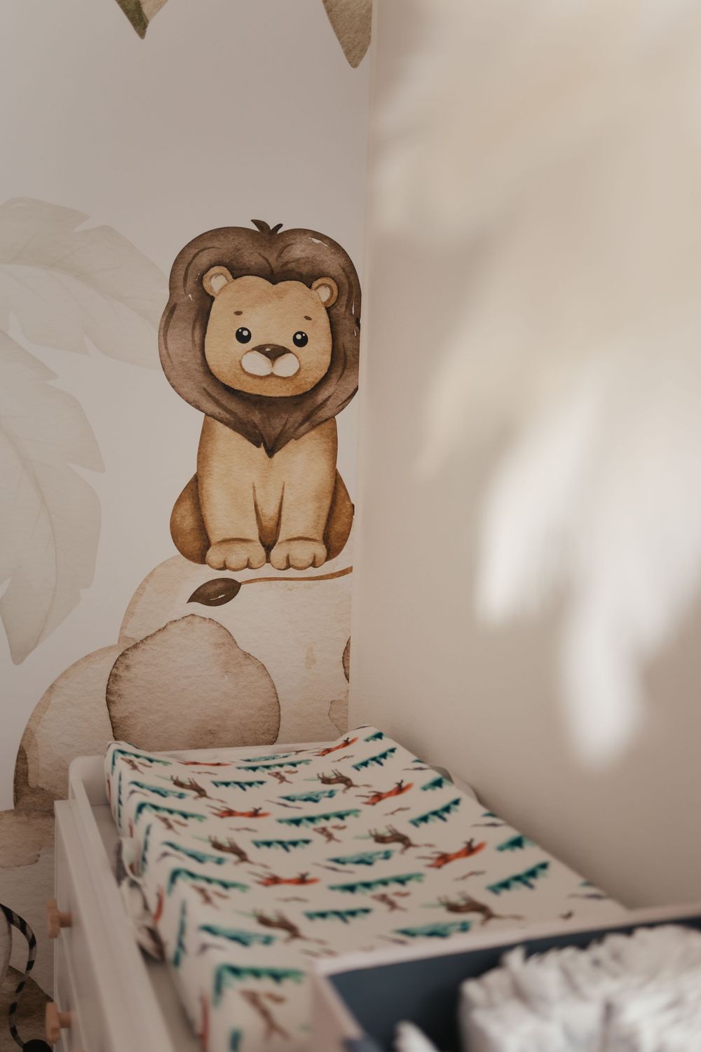 Whimsical nursery decor featuring a watercolor lion illustration above patterned bedding with a neutral beige background.