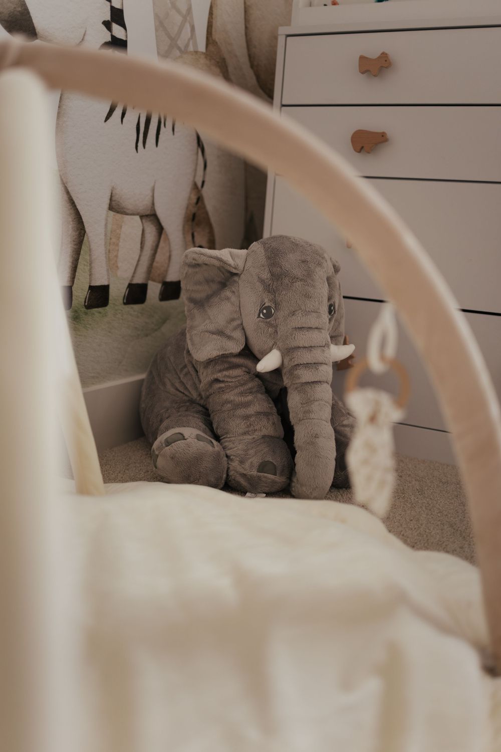 A soft gray plush elephant toy sits in a nursery corner beside a white dresser and matching décor.