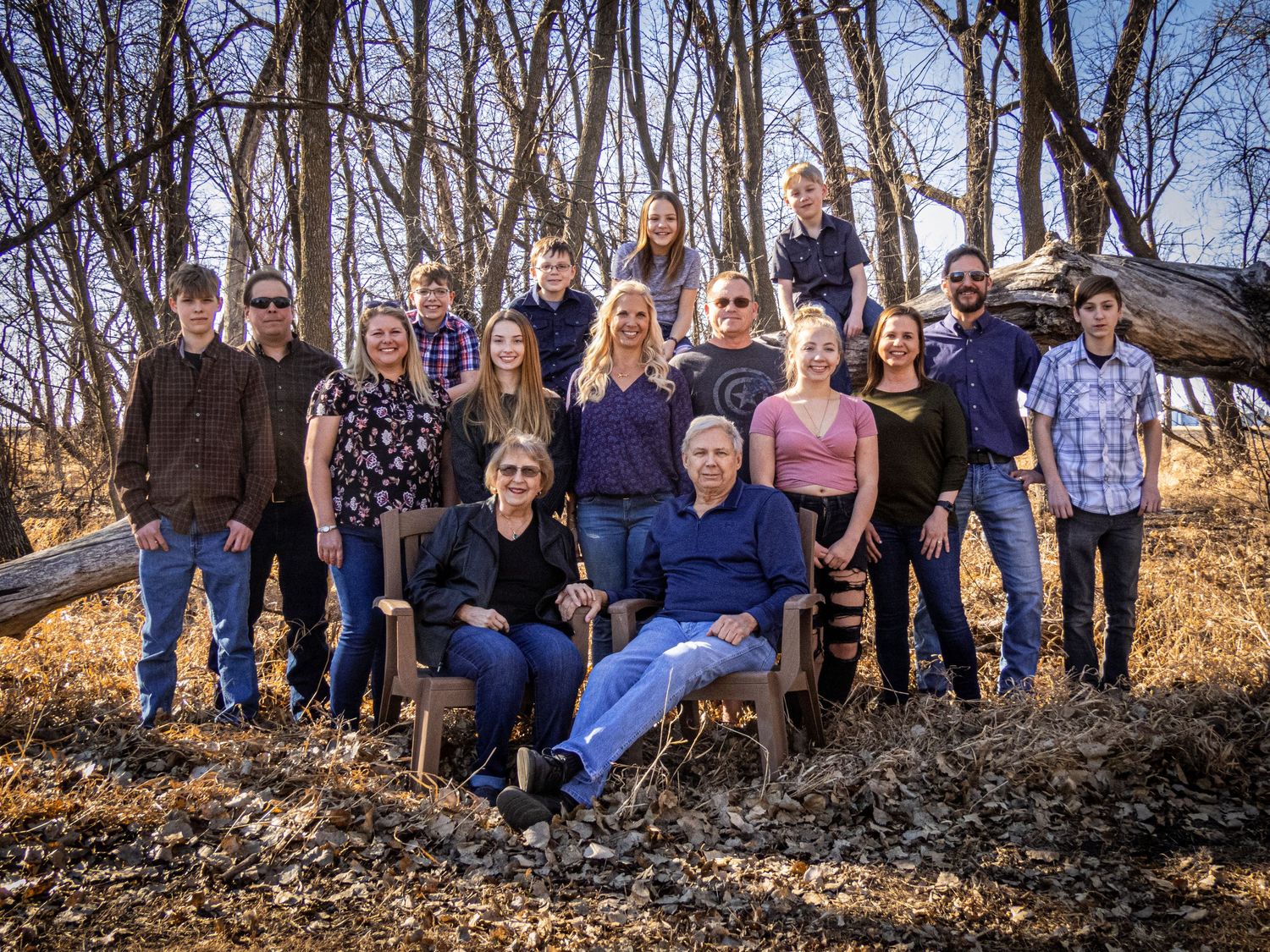 Large family group poses together outdoors among bare trees in winter setting.