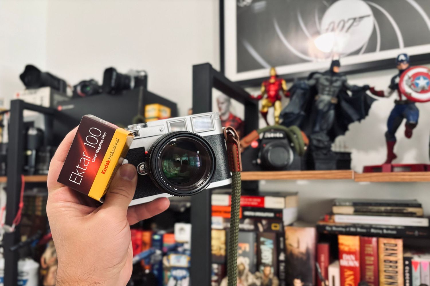 Leica camera held up against a backdrop of collectible action figures and movie memorabilia.