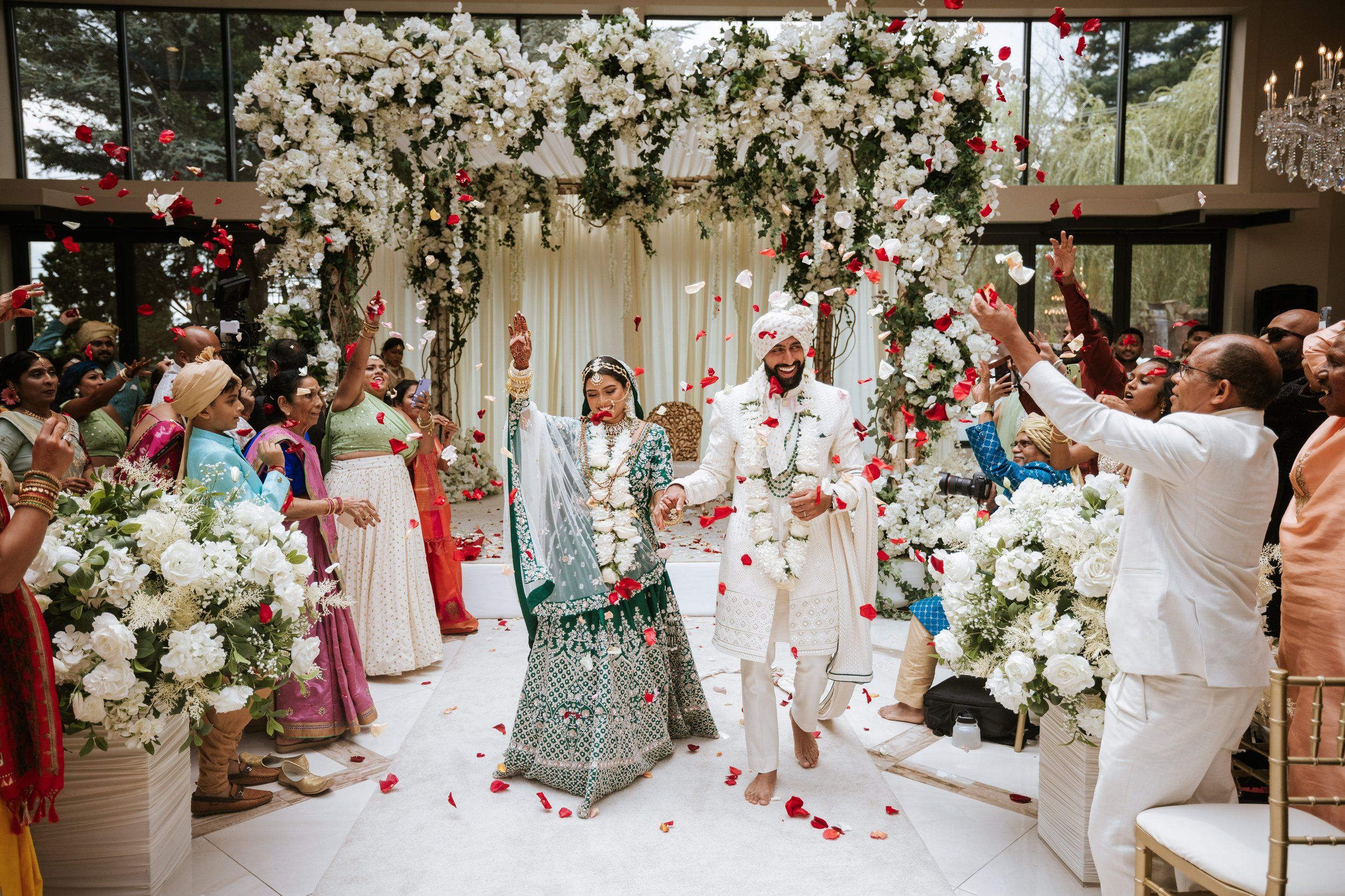 Joyful South Asian wedding exit at Lucien’s Manor — newlyweds walk under a floral mandap as guests shower petals in celebration.