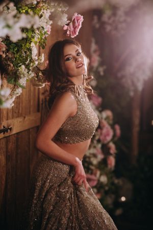 South Asian bride glows in a sparkling lehenga amidst floral decor, perfect for luxury Indian wedding inspiration and bridal portraits.