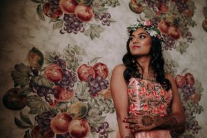 South Asian bride poses in floral lehenga against vintage fruit mural at Hilton Parsippany. Indian wedding pre-event photography.