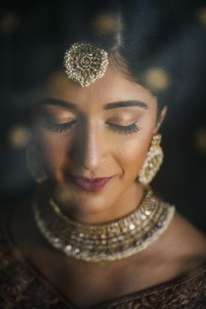 Stunning close-up of a South Asian bride in New Jersey, adorned in gold jewelry and bridal makeup, exuding elegance and serenity.
