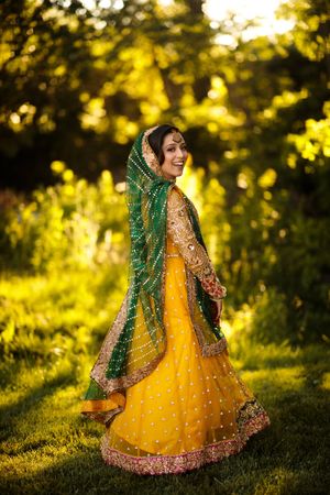 South Asian bride in a yellow lehenga twirling at golden hour outside The Marigold in Somerset, NJ, glowing in vibrant Mehndi attire.