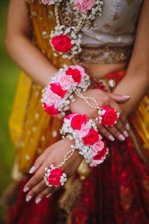 Close-up of South Asian bride's floral jewelry and henna-adorned hands, featuring pink and white blooms for the Haldi ceremony.