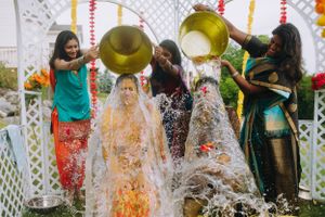 Bride enjoys a joyful Haldi ceremony at The Legacy Castle in NJ as loved ones pour water over her, surrounded by colorful festive decor.