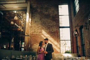Romantic engagement photo of a South Asian couple in a cozy, industrial-style restaurant in Baltimore, bathed in warm natural light.
