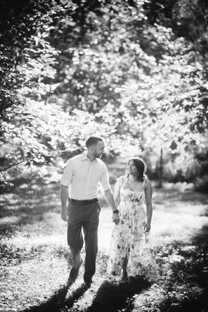 Black and white engagement photo of a couple walking hand in hand along Wissahickon Creek in Philadelphia, surrounded by nature.