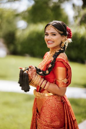 Smiling South Indian bride in traditional red saree and gold jewelry at Springfield Country Club, captured in a bright outdoor portrait.