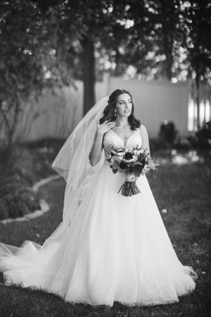 Bride in classic gown poses under trees at Springfield Country Club. Elegant black-and-white wedding portrait with timeless charm.