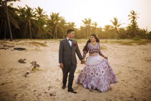 South Asian couple walking hand-in-hand on the beach at Hard Rock Punta Cana during golden hour, dressed in elegant wedding attire.