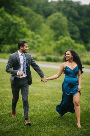 Playful engagement session at Longwood Gardens, with couple holding hands and laughing in a lush green meadow.