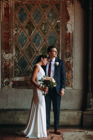Elegant wedding portrait of a couple in Central Park, NY, standing by rustic stonework with bouquet in hand and timeless style.