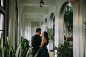 Romantic engagement photo of a South Asian couple in an elegant corridor, surrounded by greenery and natural light.