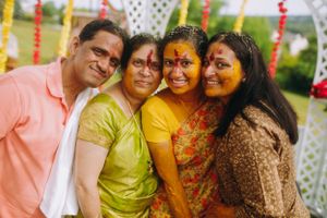 Family smiling during Haldi ceremony at Legacy Castle in NJ covered in turmeric with colorful outfits and festive decor in the background