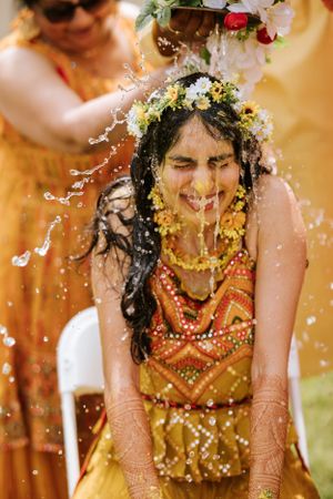 Joyful South Asian bride during Haldi ceremony at The Imperia in Franklin, NJ, covered in turmeric and floral decor, smiling brightly.