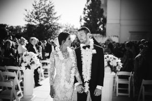 Joyful wedding recessional at The Palace at Somerset Park, couple walks hand-in-hand adorned with garlands in a black and white moment.