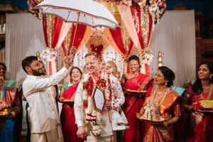 Groom showered with flower petals during vibrant South Indian wedding ceremony, surrounded by joyful family and colorful decor.