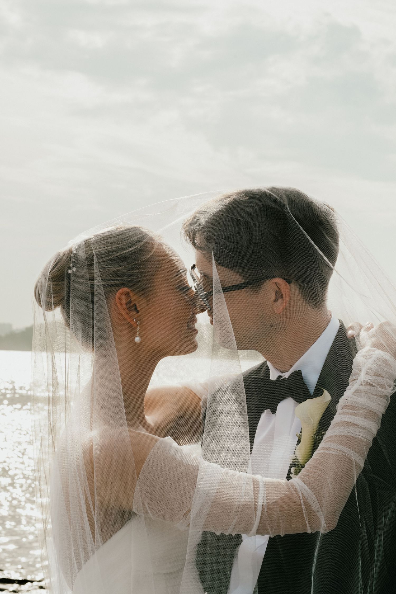 Romantic wedding portrait with veil flowing in seaside breeze at sunset.