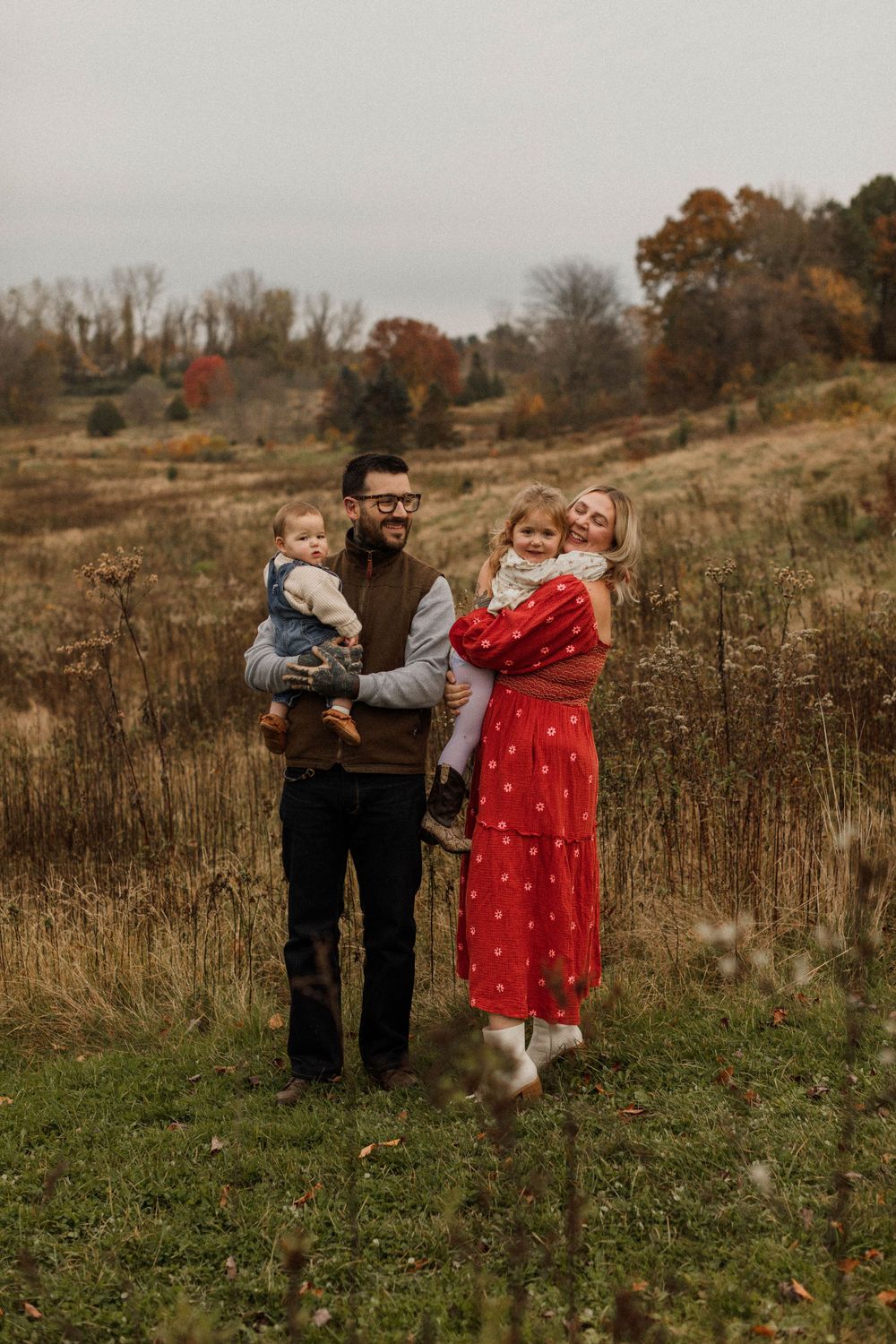 Family standing together in autumn field with golden grass and fall foliage.