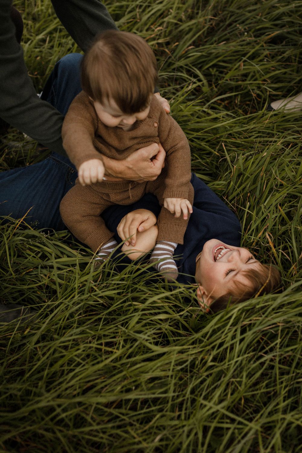 Two people playing together in tall grass during golden hour.