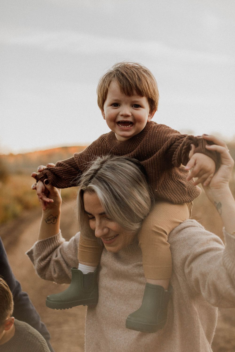 Joyful moment captured as toddler rides on parent's shoulders during autumn outdoor photo session.