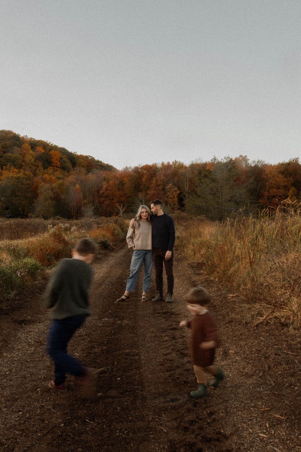 Family enjoying playful moment on autumn trail with children running ahead.