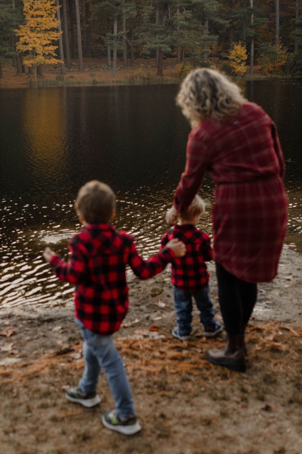 A peaceful lakeside moment with two children in buffalo plaid flannel and an adult enjoying autumn reflections.