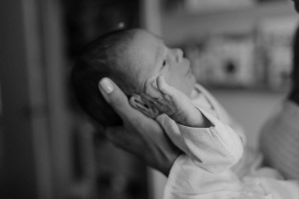 A tender black and white portrait of a newborn baby being gently cradled.