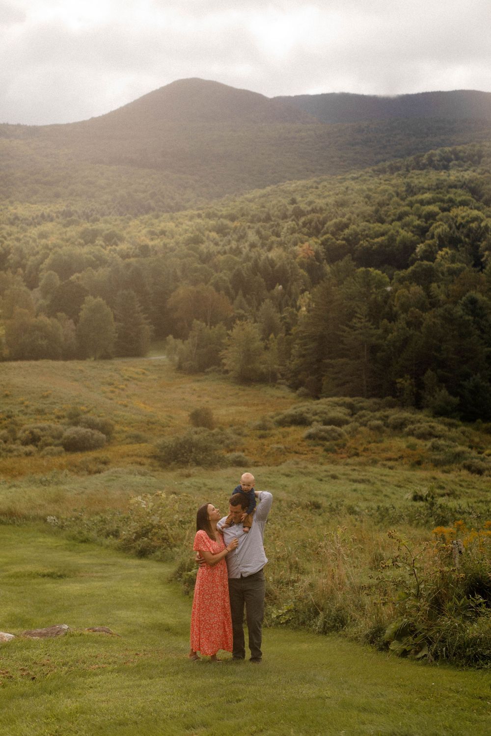 A family stands together on a hillside overlooking a scenic mountain valley.