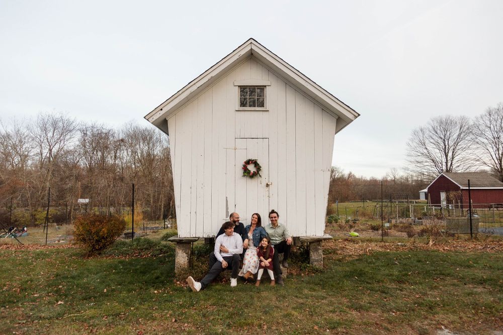 A small white outbuilding with a wreath on the door and people sitting outside.