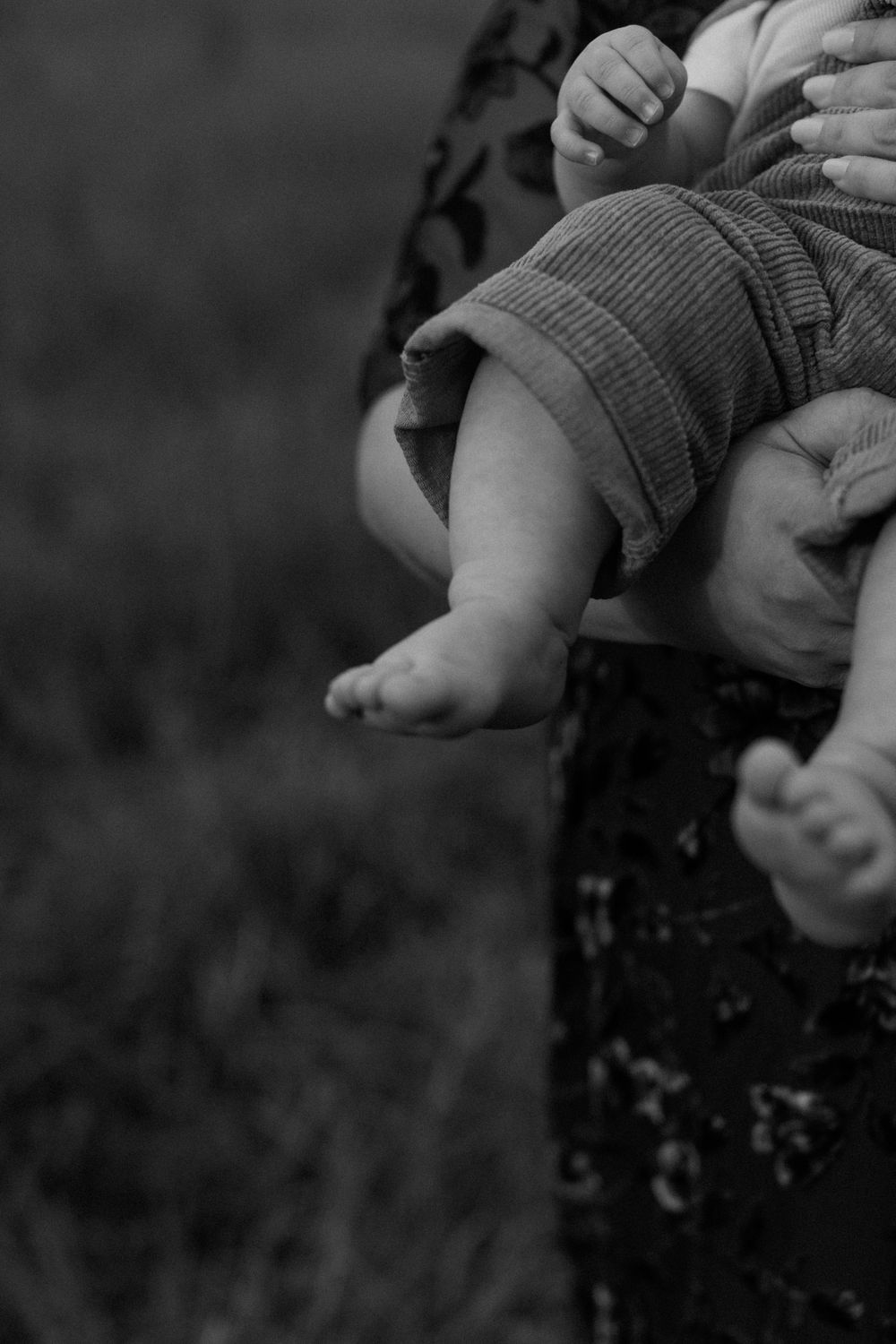 Close-up black and white photo of tiny baby feet and hands against a floral pattern.