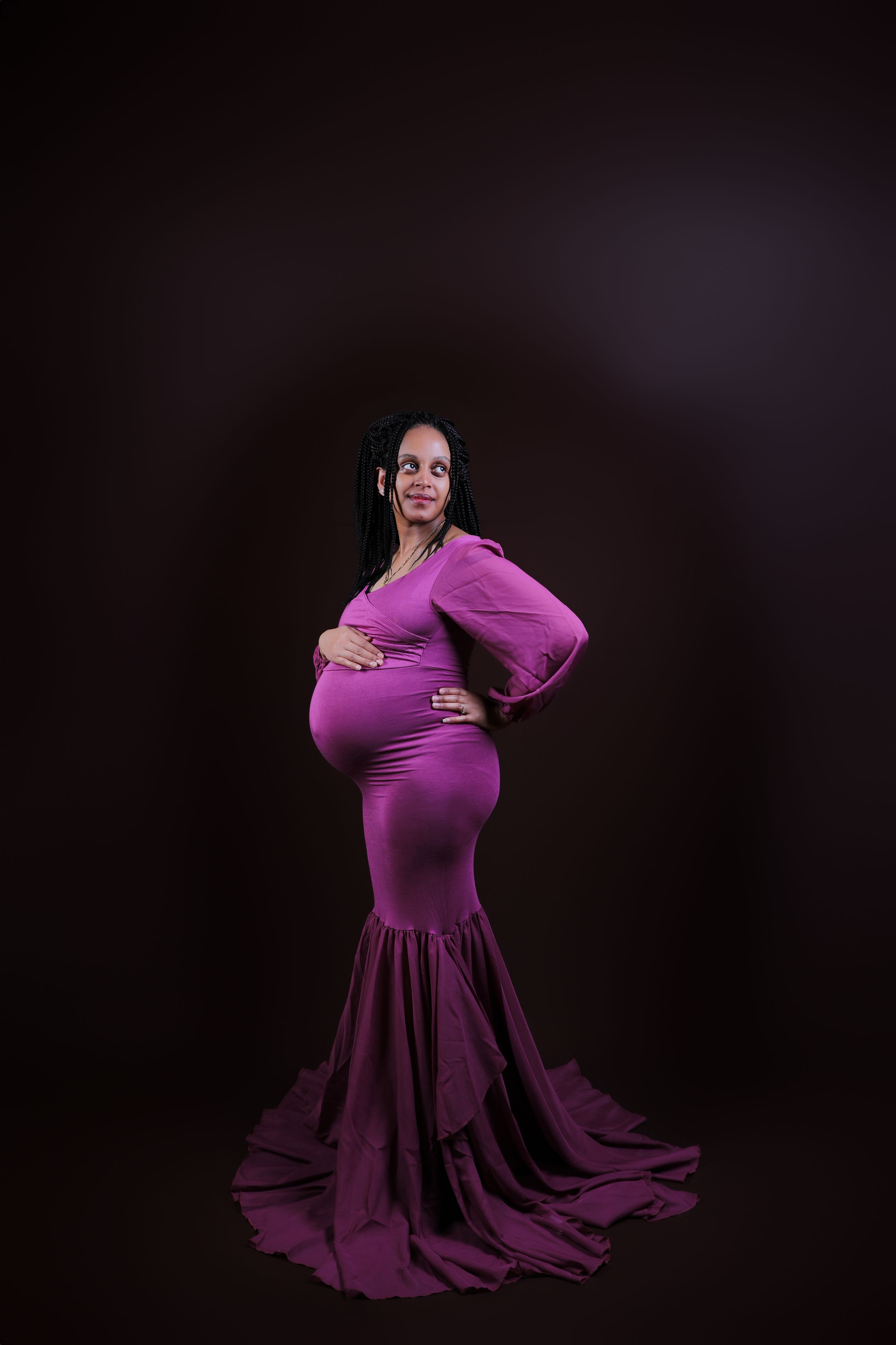 An elegant maternity photo showing a flowing purple gown against a dark backdrop.