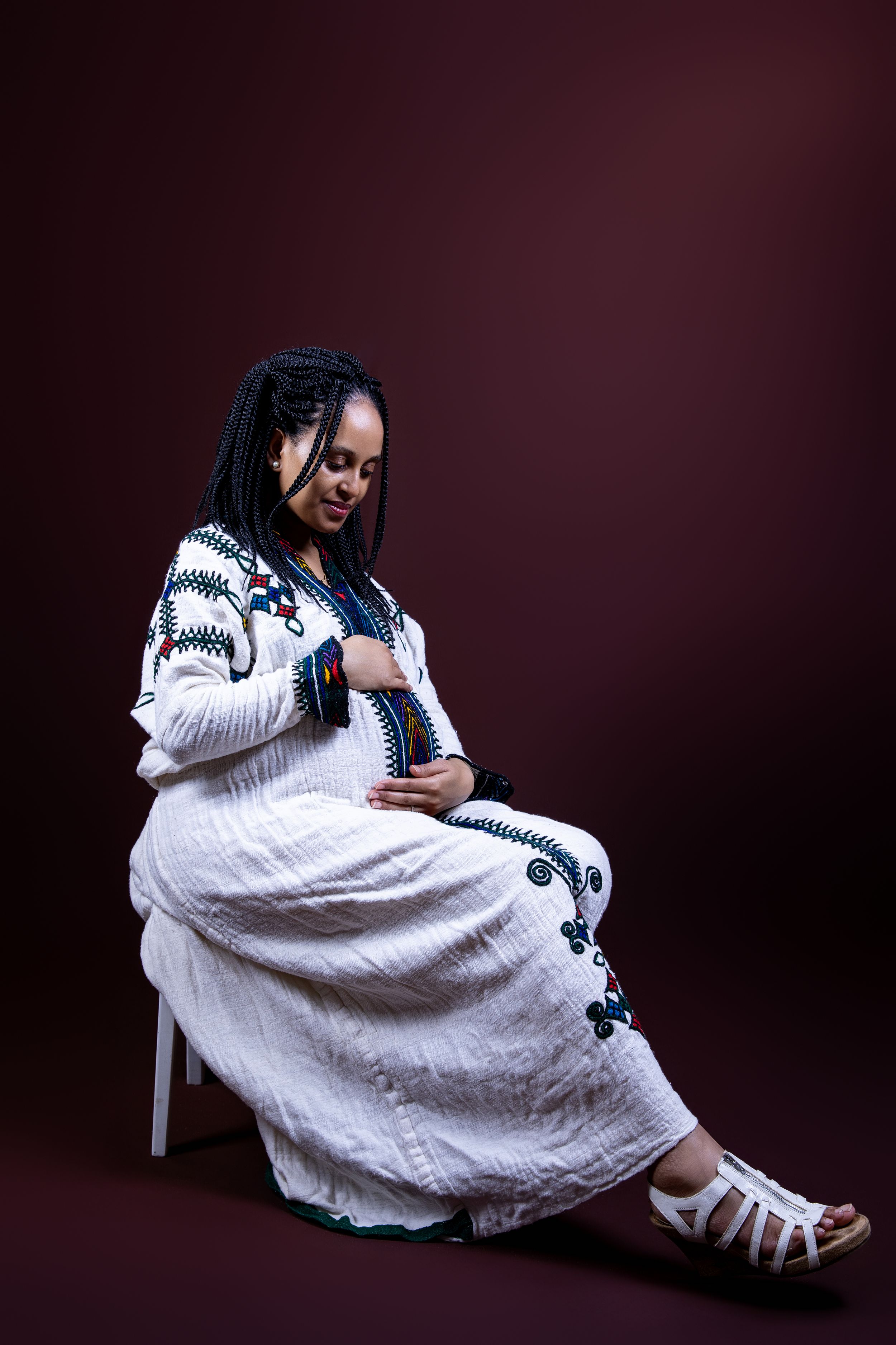 A peaceful maternity portrait in a white embroidered dress against a burgundy background.