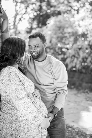 A couple shares a tender moment outdoors in black and white as they embrace during a maternity photoshoot.