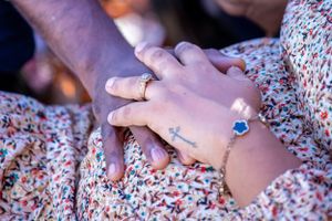 Close-up of hands with jewelry resting on a floral print dress during an intimate moment.