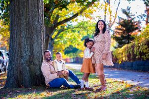 A family poses together under a large tree during autumn with golden sunlight filtering through.