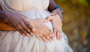 Multiple hands rest gently on a white dress forming a heart shape in soft natural lighting.