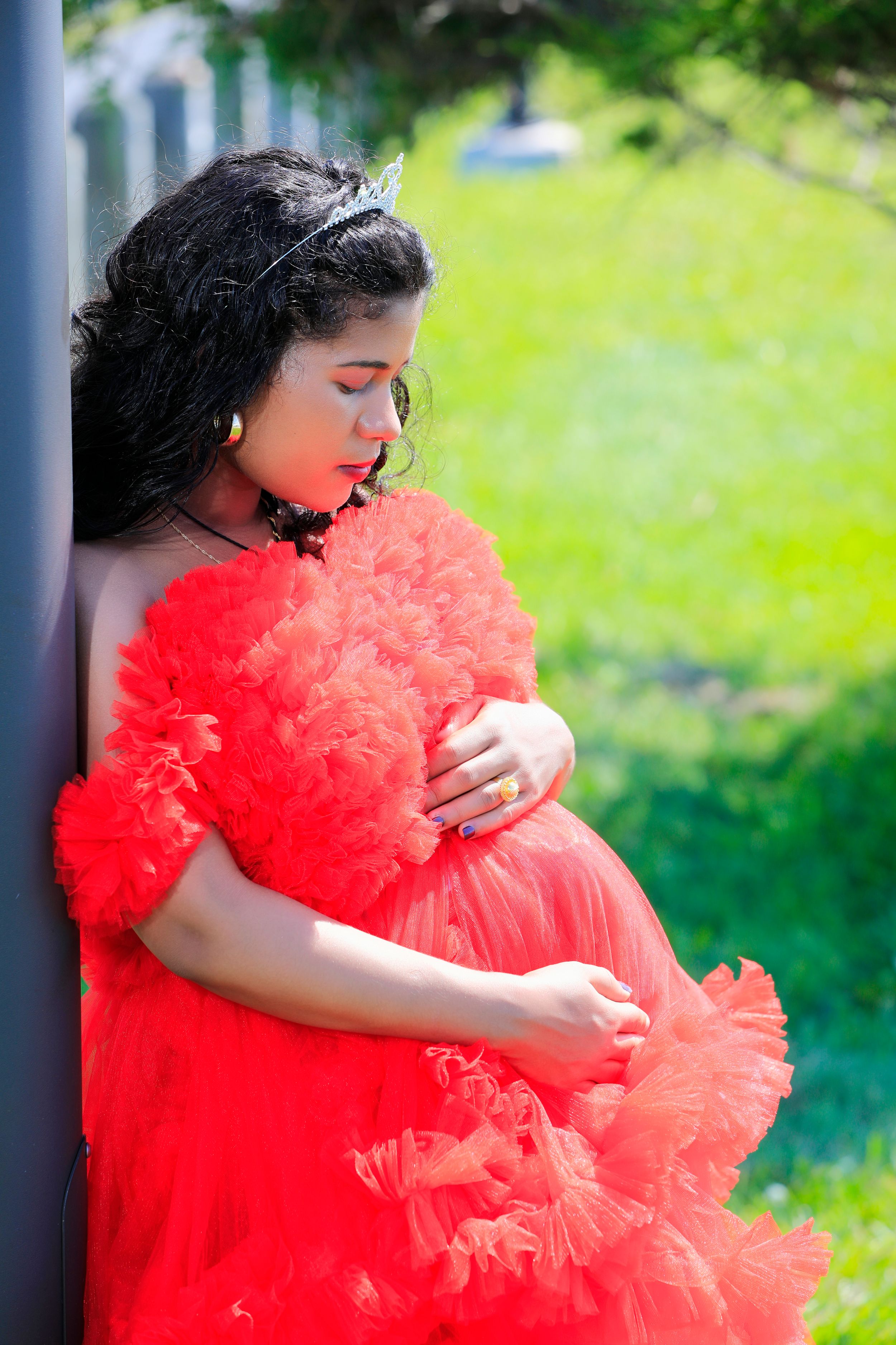 Maternity photo of woman in flowing red tulle dress against green background.