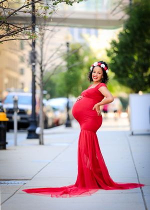 Maternity photo with woman in form-fitting red dress posing on urban sidewalk.