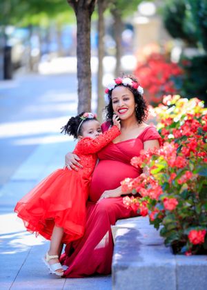 Maternity photoshoot with matching red dresses against colorful flower garden.