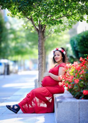 Maternity portrait session with woman in red dress sitting by blooming flowers.