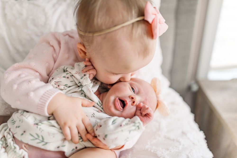 Chesterfield photographer captures toddler holding her newborn sister and giving her a kiss on the cheek.