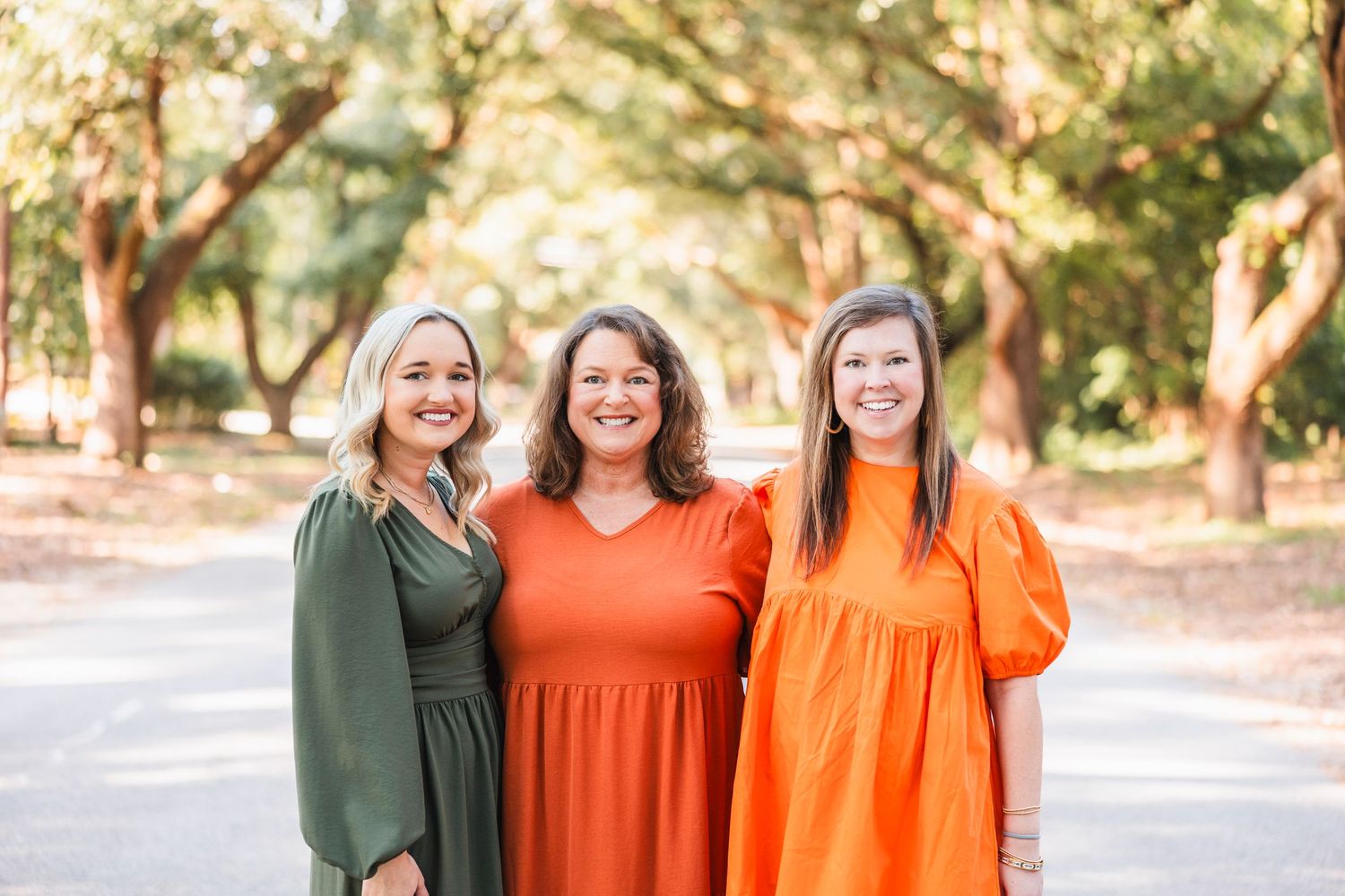 Three friends in coordinating orange and green outfits pose together outdoors during golden hour.