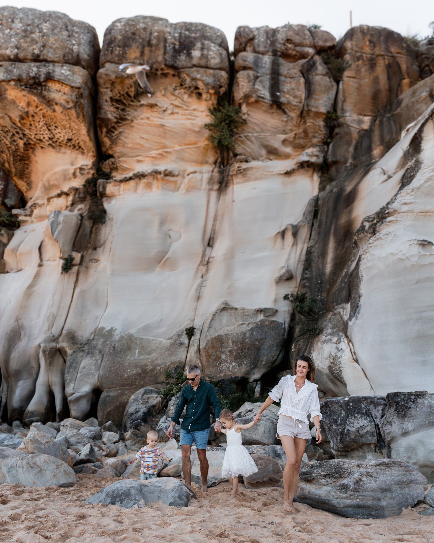 family photographer in sydney showcasing the rocks at north curl curl while the family walks in front of them
