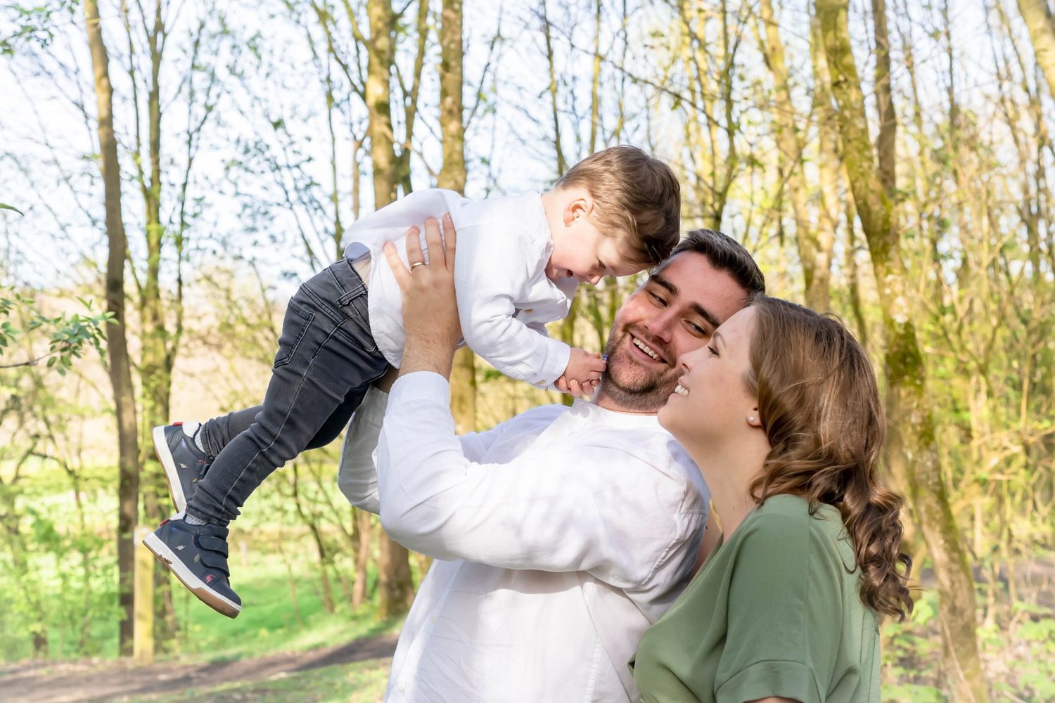 Joyful family moment outdoors with playful lifting pose in spring forest setting.